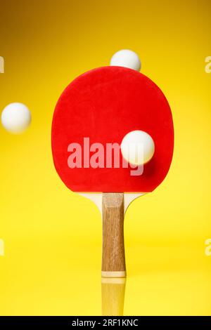 Lato rosso di una racchetta da ping pong con tre palline bianche in aria, in piedi su uno sfondo giallo. Concetto di gara di ping pong da ping pong. Foto Stock