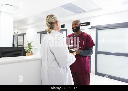 Diversi medici maschi e femmine che parlano e bevono caffè in reception in ospedale Foto Stock
