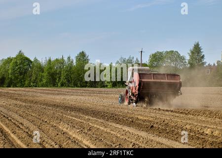 La piantatrice di patate viene agganciata al trattore durante la semina primaverile delle patate in un campo agricolo arato. Foto Stock