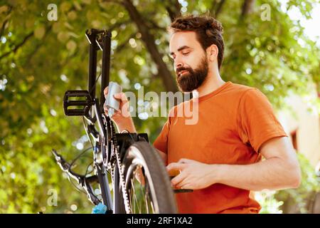 Uomo sportivo e dedito che utilizza un lubrificante specializzato per ingrassare la sua catena di biciclette. L'immagine mostra un uomo caucasico che lubrifica abilmente l'anello della catena della sua moto per un'esperienza ciclistica senza interruzioni. Foto Stock