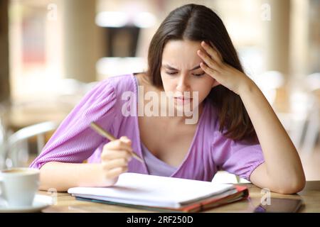 Studente stressato che studia le note più dure in una terrazza del bar Foto Stock