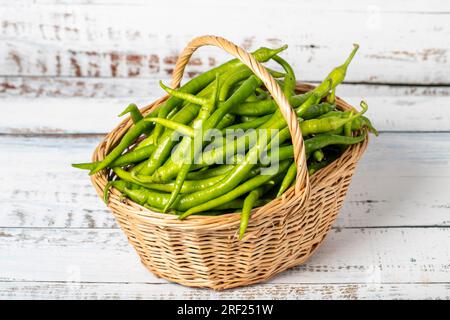 Pepe verde fresco in un cestino di vimini su sfondo di legno. Concetto di stagione di raccolta del peperoncino verde. Verdure per una dieta sana Foto Stock