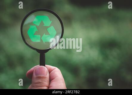 Concetti di riduzione dei rifiuti, inquinamento, riutilizzo, uso efficiente delle risorse. Proteggere l'ambiente riciclando. Mano umana che regge una lente d'ingrandimento Foto Stock