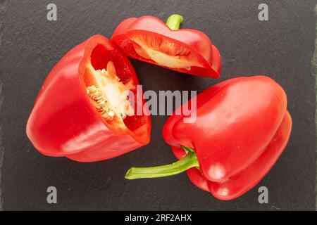 Una metà intera e due metà di pepe rosso dolce su pietra di ardesia, macro, vista dall'alto. Foto Stock