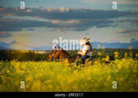 Ragazza che cavalca in un campo di canola nel Montana Foto Stock