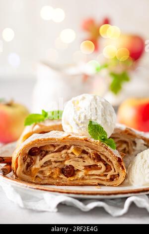 Pezzi tradizionali di strudel di mele con cannella, uva passa, zucchero in polvere e gelato alla vaniglia. Foto Stock