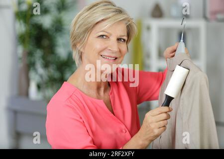 donna matura che si rimuove la lanugine dalla giacca Foto Stock