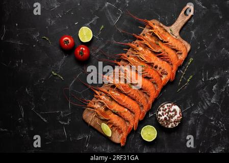 Grandi langoustine su una tavola di legno, sfondo in pietra nera. Vista dall'alto, base piatta. Langoustina bollita rossa. Foto Stock