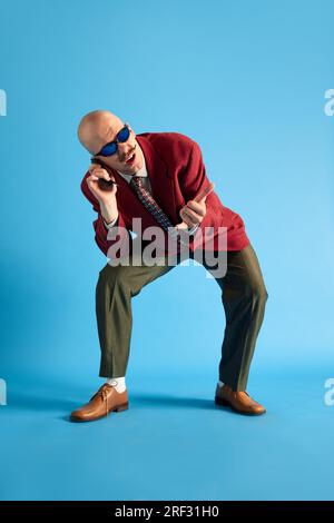 Uomo dalle pieghe con baffi, in stile vintage, piegato su un telefono retrò con indicazione della chiamata su sfondo blu. Foto Stock