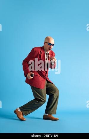 Immagine a tutta lunghezza. Uomo balsamato con baffi vestito in abito retrò professionale che si sovrappone a uno sfondo blu da studio. Foto Stock