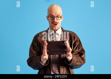 Immagine di un giovane uomo calvo e baffi sorpreso in occhiali con scatola in mano su sfondo blu da studio. Foto Stock