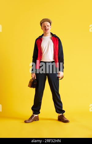 Immagine di un giovane allenatore sportivo vestito con abbigliamento sportivo e con borsetta e berretto sullo sfondo giallo brillante dello studio. Foto Stock
