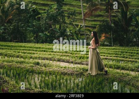 Bella ragazza in abito verde che cammina sulla terrazza di riso. Signora elegante in visita alla piantagione di riso Foto Stock