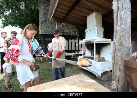 KIEV, UCRAINA - 29 LUGLIO 2023 - un dipendente della panetteria artigianale From Grain to Bread prende i panini dal forno con una buccia e li mette sul t Foto Stock