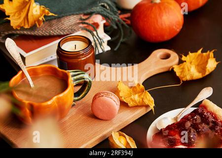 Estetica tazza di caffè autunnale a forma di zucca, macaron, torta di ciliegie, zucche, candela. Primo piano sfocato. Tempo caffè atmosferico. Foto Stock