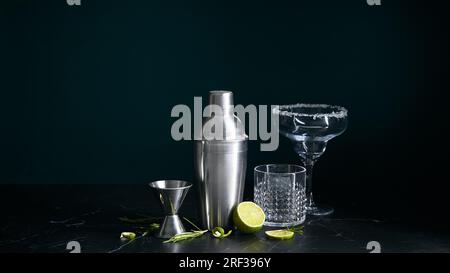 Shaker da cocktail e bicchieri da cocktail e ingredienti su fondo di marmo scuro. Foto Stock