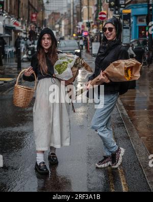 Due signore che portano fiori abbracciano il tempo piovoso di Londra. Foto Stock