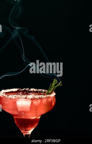 Cocktail tipo margarita alcolico o analcolico con ghiaccio e rametto di rosmarino fumante su fondo scuro. Foto Stock