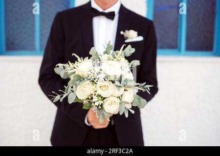 Stilvoller Bräutigam wartet vor der Kirche auf die Braut mit einem Blumenstrauß Foto Stock