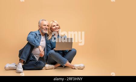 Felice coppia di anziani che usa un notebook, guardando lo spazio vuoto Foto Stock