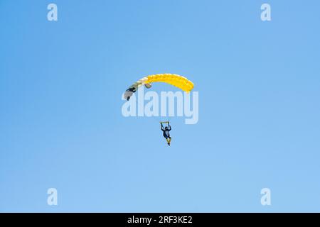 Vista mozzafiato di un paracadutista con un paracadute giallo e un cielo blu sullo sfondo. Foto Stock