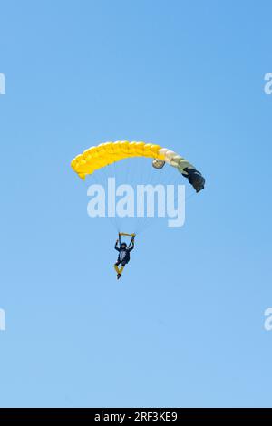 Vista mozzafiato di un paracadutista con un paracadute giallo e un cielo blu sullo sfondo. Foto Stock