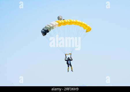 Vista mozzafiato di un paracadutista con un paracadute giallo e un cielo blu sullo sfondo. Foto Stock