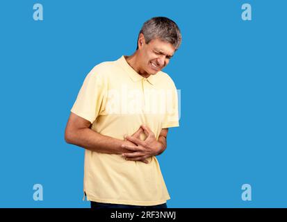 Uomo maturo che soffre di mal di stomaco che tocca lo stomaco su sfondo blu Foto Stock