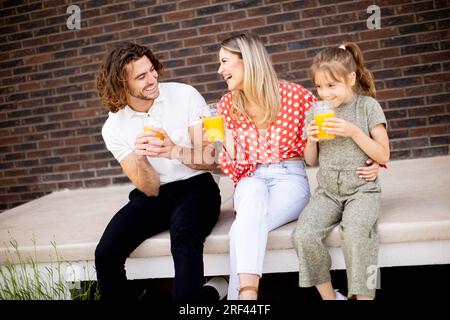 Famiglia con una madre, un padre e una figlia seduti fuori sui gradini di una veranda anteriore di una casa in mattoni Foto Stock