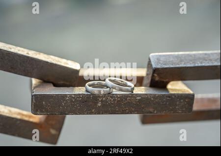 Due mani con anelli nuziali poggiano su una robusta catena di ancoraggio. Foto Stock