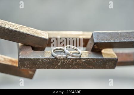 Due mani con anelli nuziali poggiano su una robusta catena di ancoraggio. Foto Stock