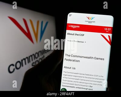 Persona in possesso di un cellulare con pagina Web dell'organizzazione Commonwealth Games Federation (CGF) sullo schermo con logo. Concentrarsi sul centro del display del telefono. Foto Stock