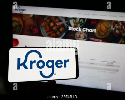 Persona in possesso di un cellulare con il logo dell'azienda statunitense al dettaglio The Kroger Company sullo schermo davanti alla pagina Web. Concentrarsi sul display del telefono. Foto Stock