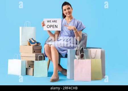 Venditore femminile con cartello di apertura, scatole di scarpe e borse della spesa su sfondo blu Foto Stock
