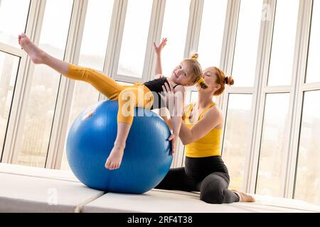 Mamma e figlia giovani si divertono con la palla fitness in palestra Foto Stock