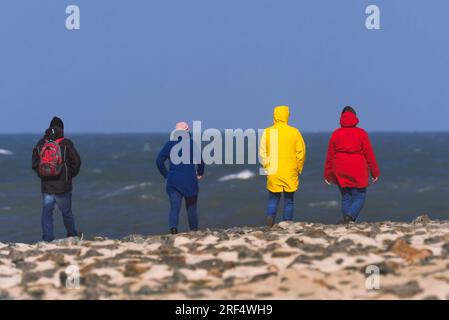 Wangerooge, Germania. 11 aprile 2023. 11.04.2023, Wangerooge. Le persone in abiti colorati e funzionali camminano sulla riva del Mare del Nord sull'isola frisone orientale di Wangerooge. Credito: Wolfram Steinberg/dpa credito: Wolfram Steinberg/dpa/Alamy Live News Foto Stock