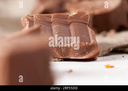 cioccolato al latte commestibile a base di cacao e zucchero, pezzi di cioccolato sparsi casualmente sul tavolo, cioccolato naturale rotto e sbriciolato Foto Stock