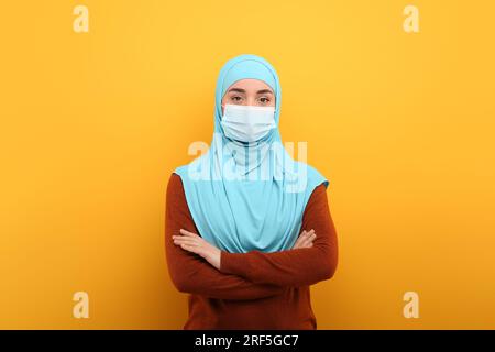 Ritratto di donna musulmana in hijab e maschera medica su sfondo arancione Foto Stock