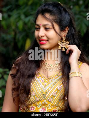 Splendida donna con lunghi capelli ricci che indossa ghaghra e choli gialli e orecchini a forma di Diya e gioielli per il matrimonio indiano. Orecchino a forma di lampada. Foto Stock