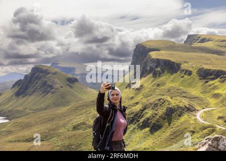 Giovane donna che fa selfie con lo smartphone sulla catena montuosa di Quiraing. È una formazione geologica sull'isola scozzese di Skye e un paradiso per gli escursionisti Foto Stock