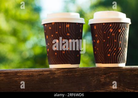 Due tazze di caffè in cartone ondulato su un balcone in legno, luce naturale, sfondo sfocato. Sconti per il negozio di bevande: Banner per la vendita di bevande calde. Promozione promozionale de Foto Stock