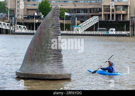 Londra, Regno Unito. Agosto 2023. Un kayak passa una delle tre pinne giganti di squalo Megalodon che sembrano salire sulla superficie del Tamigi vicino al Tower Bridge per promuovere la pubblicazione nel Regno Unito, il 4 agosto, della Warner Bros. Film di immagini "Meg 2: The Trench", con Jason Statham. Secondo il Museo di storia naturale, la specie preistorica conosciuta come Otodus megalodon era lo squalo più grande del mondo e uno dei pesci più grandi mai esistiti. Crediti: Stephen Chung / Alamy Live News Foto Stock