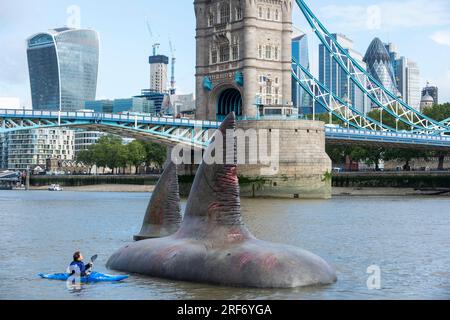 Londra, Regno Unito. Agosto 2023. Un kayaker passa due delle tre pinne giganti di squalo Megalodon che sembrano salire sulla superficie del Tamigi vicino al Tower Bridge per promuovere l'uscita nel Regno Unito, il 4 agosto, della Warner Bros. Film di immagini "Meg 2: The Trench", con Jason Statham. Secondo il Museo di storia naturale, la specie preistorica conosciuta come Otodus megalodon era lo squalo più grande del mondo e uno dei pesci più grandi mai esistiti. Crediti: Stephen Chung / Alamy Live News Foto Stock