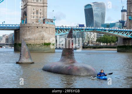 Londra, Regno Unito. Agosto 2023. Un kayaker passa due delle tre pinne giganti di squalo Megalodon che sembrano salire sulla superficie del Tamigi vicino al Tower Bridge per promuovere l'uscita nel Regno Unito, il 4 agosto, della Warner Bros. Film di immagini "Meg 2: The Trench", con Jason Statham. Secondo il Museo di storia naturale, la specie preistorica conosciuta come Otodus megalodon era lo squalo più grande del mondo e uno dei pesci più grandi mai esistiti. Crediti: Stephen Chung / Alamy Live News Foto Stock