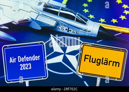 FOTOMONTAGE, Militärjetmodell auf NATO-Fahne und Schilder mit Aufschrift Fluglärm und Air Defender 2023, Symbolfoto NATO-Luftmanöver Foto Stock