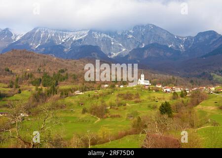 Vista panoramica del villaggio di Drežnica vicino a Kobarid, Slovenia, con le montagne delle alpi Giulie coperte di nuvole e i prati sotto il sole Foto Stock
