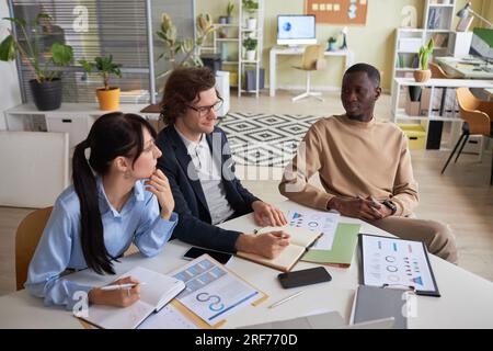 Vista dall'alto in un team di giovani imprenditori composto da tre persone sedute al tavolo da riunione in ufficio e brainstorming di idee di progetto, spazio copia Foto Stock