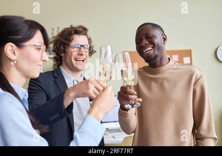 Ritratto di tre colleghi che indossano bicchieri di champagne in ufficio e che ridono felici durante la festa in ufficio Foto Stock
