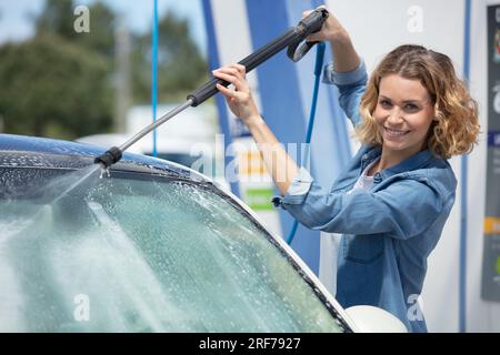 giovane donna che pulisce la sua auto in una cabina self service Foto Stock