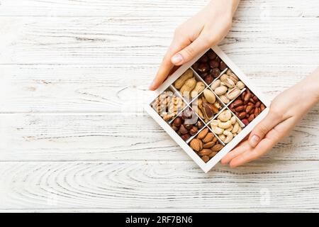 Giovane donna che tiene scatola con noci diverse, primo piano. Primo piano, spazio di copia, vista dall'alto, disposizione piatta. Noce, pistacchi, mandorle, nocciole e anacardi. Foto Stock